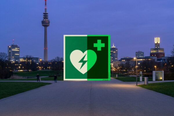 Großes grünes AED-Defibrillator-Symbol über der Skyline von Dortmund im Westfalenpark bei Dämmerung mit Florianturm und Dortmunder U.
